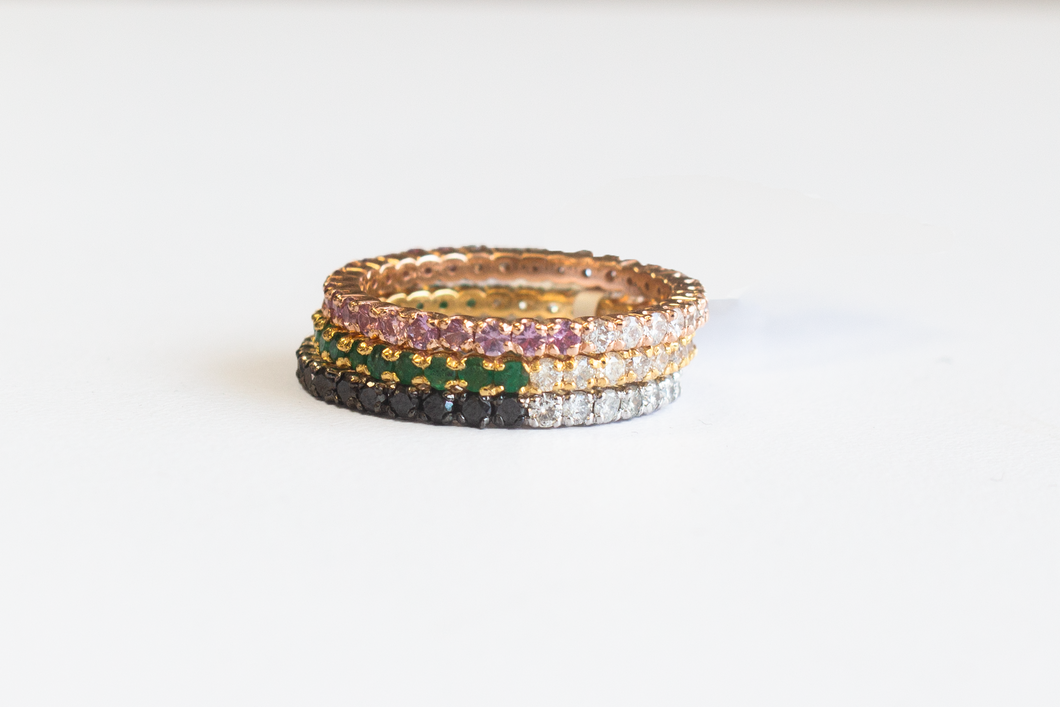 Three 14k yellow and white gold half and half eternity bands with diamonds and colored gems sstacked atop one another on a whtie background.