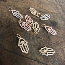Load image into Gallery viewer, Numerous Diamond Hamsa Pendants in 14K yellow, rose and whiteGold laid flat on a wooden background.
