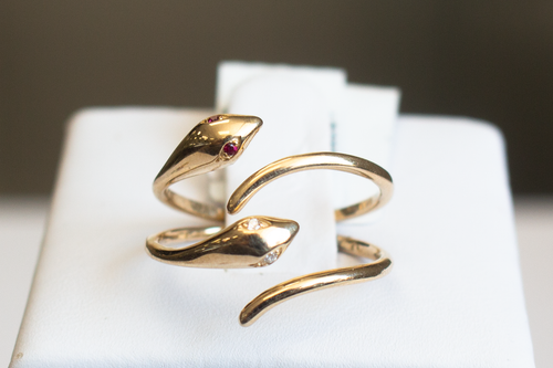 Two Snake Wrap 14k Yellow Gold Rings with ruby and diamond eyes stacked on a ring stand on a white background.